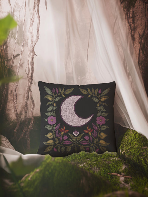 Black woven throw pillow with an embroidered crescent moon and floral pattern in soft ivory, green, purple, and gold, featuring a textured finish.